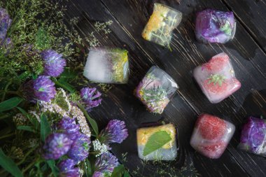 İyileştirici otlarla kaplı buz küpleri yonca çiçekleri olan ahşap bir masanın arka planına yakın.