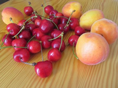 Hafif ahşap masada taze yaz meyveleri. Ahşap zemin üzerinde kayısı ve kiraz