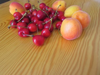 Hafif ahşap masada taze yaz meyveleri. Ahşap zemin üzerinde kayısı ve kiraz