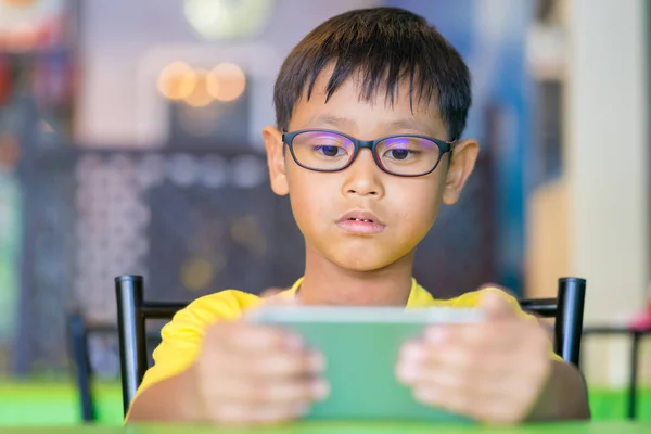 A Smart Phone holding / watching in hand of asian children wearing glasses that block blue light , Technology smartphone background concept