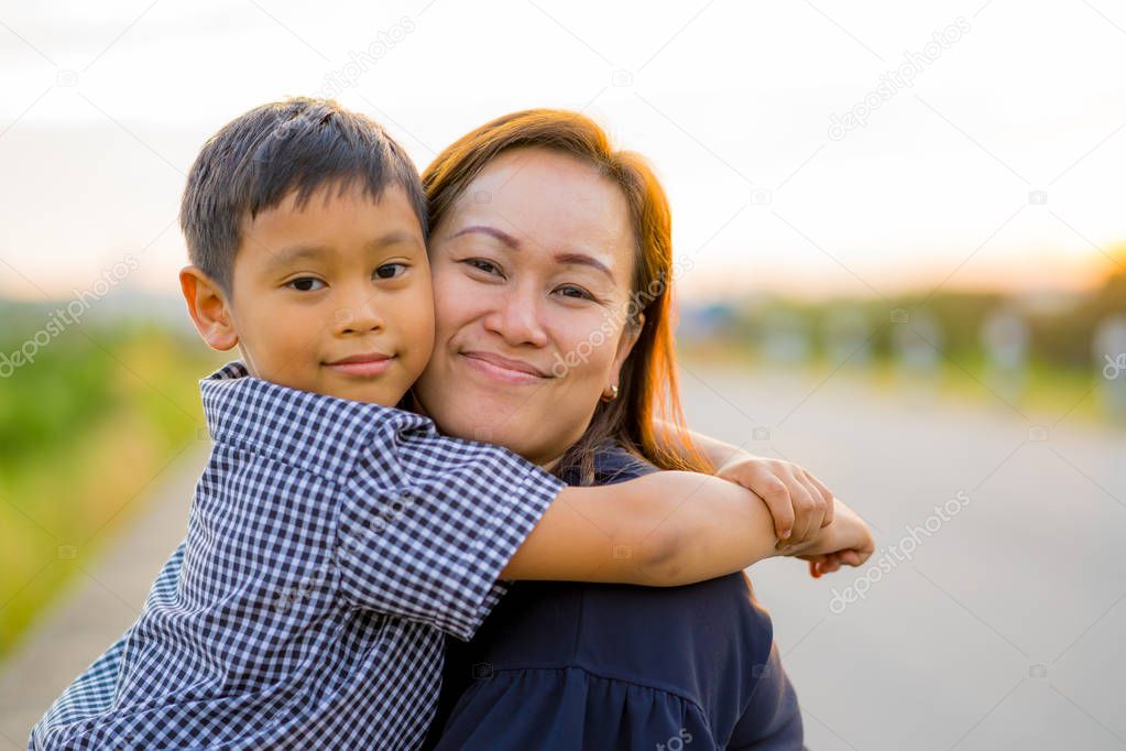 Asian mom hug her young son lovingly at sunset with nature backg
