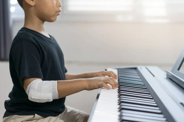 En asiatiska pojkar på sårade händerna spelar piano. — Stockfoto