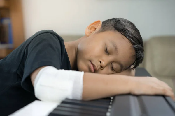 Um asiático meninos no ferido mãos são dormir no piano . — Fotografia de Stock