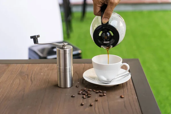 People pouring coffee in  cup beside Coffee grinder