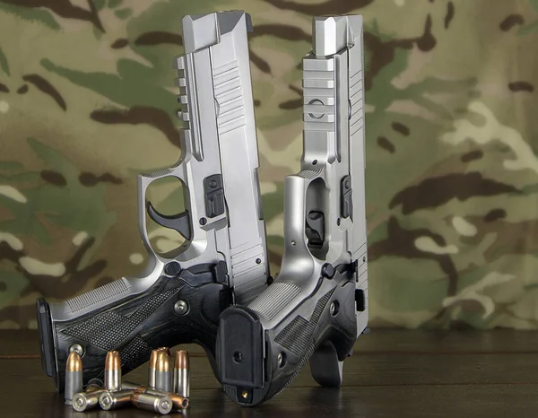 semi-automatic pistols with cartridges on a camouflage background. the image clearly shows the cartridges, barrel, bolt, handle and texture of the material of the weapon