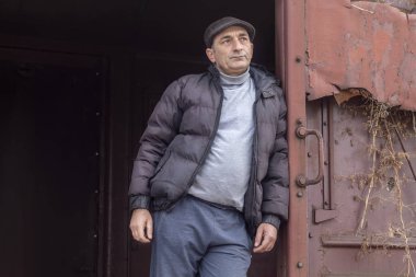 Orta Çağ Adamı Terk Edilmiş Tren Vagonu 'nun Açık Kapısı' na yaslanıyor ve Mesafeye Bakıyor