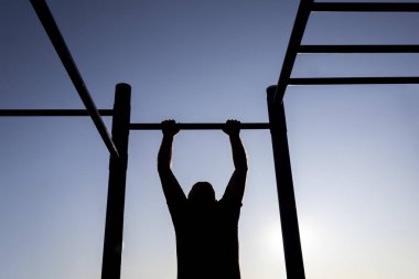 Gün batımında oyun sahasındaki barda egzersiz yapan adamın silueti.