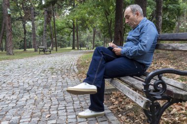 Park 'taki ahşap bankta oturan ve not alan orta yaşlı bir adam.