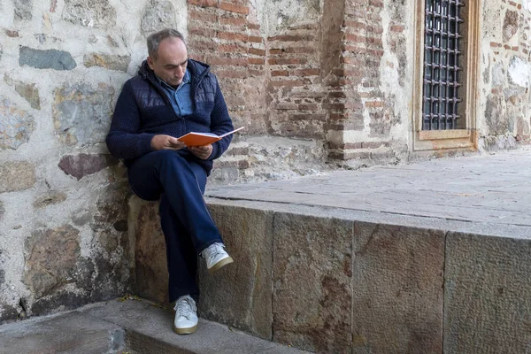 Men Leaning on Ancient Brick Wall and Sitting on Ancient Stone Wall Holding and Reading Book