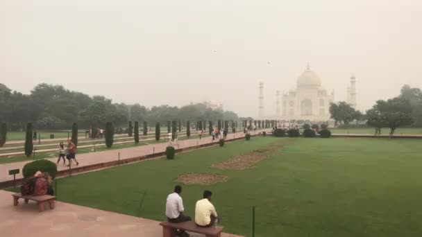Агра, Индия, 10 ноября 2019 года, Тадж-Махал, туристы сидят на лавочке у ограждения — стоковое видео