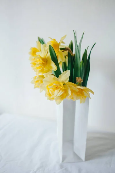 Boeket van narcissus in een papieren zak. Bloemen bezorgen. Gele bloemen in het voorjaar. Pasen boeket. Eco-verpakking te bewaren. Bloemen uit de tuin. Bloemen op tafel. Witte tabel. Ethno stijl. Verkoop van bloemen. — Stockfoto