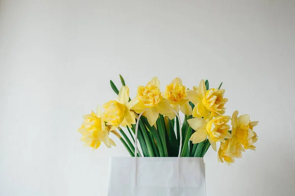 Boeket van narcissus in papieren zak. Bloemen bezorgen. Gele bloemen in het voorjaar. Pasen boeket. Eco-verpakking. Bloemen uit de tuin. Bloemen op tafel. Witte tabel. Ethno stijl. Verkoop bloemen. Mother's day. — Stockfoto