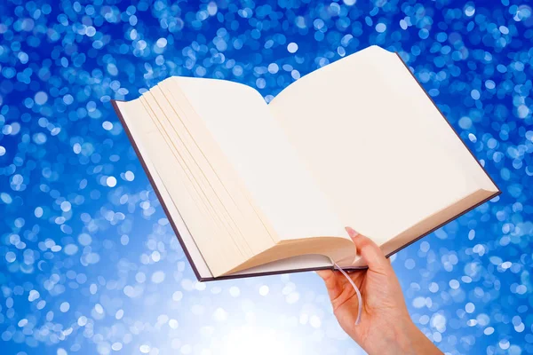 Mão feminina segurando um livro isolado no fundo azul — Fotografia de Stock