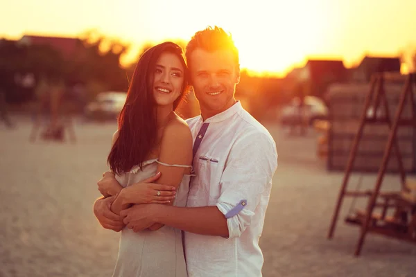 Modisches junges Paar, das am Strand steht und in einem weißen Kleid posiert, das bei Sonnenuntergang Liebe zeigt. mit benutzerdefiniertem Weißabgleich, Farbfiltern und etwas feinem Filmrauschen — Stockfoto