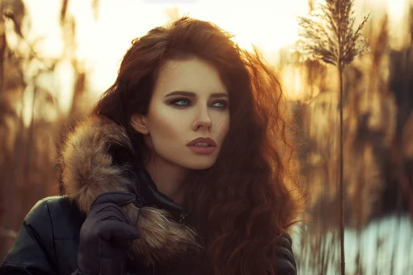 Fashion street style look casual clothes for woman walking at park, warm texture black jacket with fur hood beautiful sexy model, pretty face, redhead model luxury lifestyle winter sunset background — Stock Photo, Image