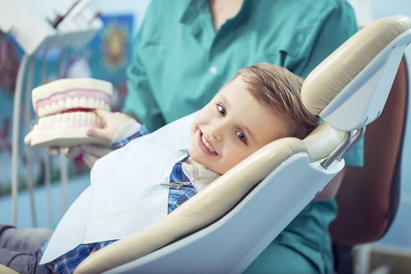 Niño muy feliz después de que el médico en la clínica, sosteniendo una mandíbula dental en sus manos y tener una hermosa sonrisa blanca. Copiar espacio — Foto de Stock