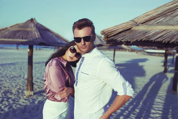 Sunset bulvarında deniz kenarında oturan genç mutlu şık çift. Adam ve kadın romantik seksi yaz giysileri ve şık moda güneş gözlüğü takmış