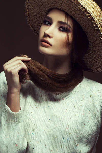 Hipster style. Fashionable portrait of a young beautiful girl wearing trendy white  knitted pullover and straw hat, posing over retro chocolate background. Vogue style. Studio shot — Stock Photo, Image