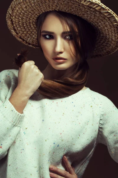 Hipster style. Fashionable portrait of a young beautiful girl wearing trendy white  knitted pullover and straw hat, posing over retro chocolate background. Vogue style. Studio shot — Stock Photo, Image