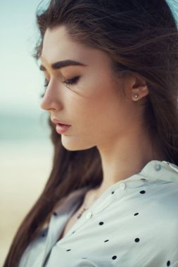 Deniz kıyısında poz beyaz puantiyeli gömlek genç ve yakışıklı bir kadın portresi. Yakın çekim. Deniz/plaj moda kavramı. 