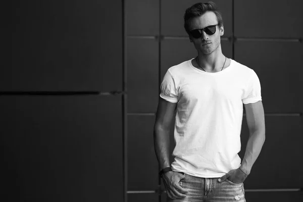 Street fashion concept. Portrait of a young and handsome man in a white t shirt and trendy glasses posing over black modern background. Close up. Street shot. copy space — Stock Photo, Image
