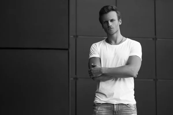 Conceito de moda de rua. Retrato de um homem jovem e bonito em uma camiseta branca e óculos da moda posando sobre fundo moderno preto. Fecha. Tiro na rua. espaço de cópia — Fotografia de Stock