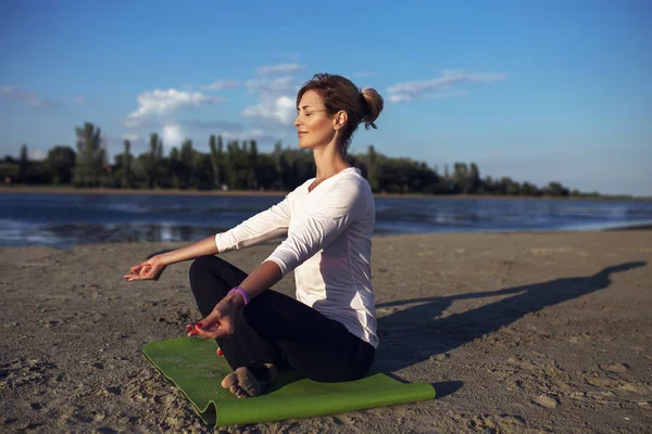 Woman practices yoga and meditates in the lotus position on the beach — Stock Photo, Image