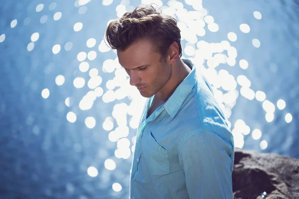 Retrato de um homem jovem e bonito em uma camisa de aqua e calças leves. Caminhando pelo mar e rochas marinhas. Conceito de moda mar / praia . — Fotografia de Stock