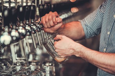 Bira döküyor. Genç barmen dökme bira kupa için kırpılmış görüntü.