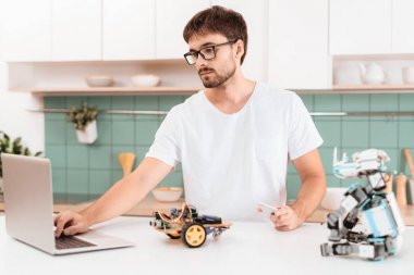 Gözlüklü bir adam mutfakta anlamına gelir ve bir robot programlama devreye girer. Yakında o çalıştığı bir dizüstü bilgisayar ve bir gergedan bir robottur. Modern bir ışık mutfakta olduklarını.