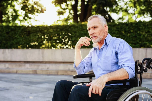 Starý muž sedí na vozíku v parku — Stock fotografie