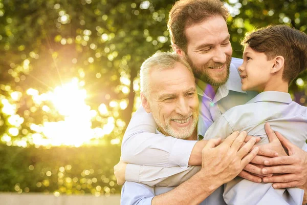 Reunión familiar. Un hombre y un niño vinieron a ver a su abuelo que se sienta en un parque en una silla de ruedas — Foto de Stock