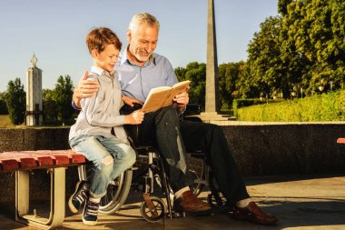 Yaşlı bir adam bir şey bir kitapta onun torunu için gösterir. Yaşlı adam bir tekerlekli sandalye üzerinde oturan