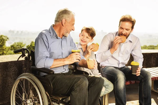 Ο γέρος σε μια αναπηρική καρέκλα, ο γιος του και ο εγγονός του τρώνε στο πάρκο — Φωτογραφία Αρχείου