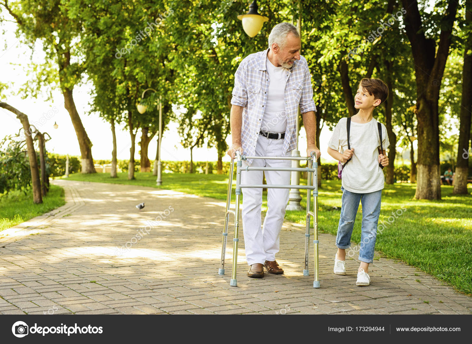 A boy and an old man on stilts for adults are walking in the park - Main Image