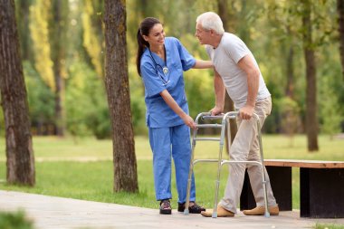A nurse helps a pensioner to walk in the park on adult stilts