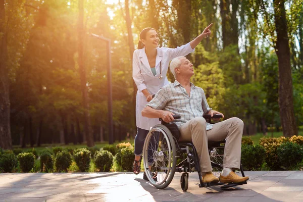 Doctor mostrar algo de interés a anciano en silla de ruedas — Foto de Stock