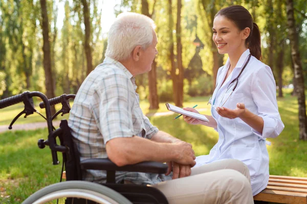 Doktorn med en anteckningsbok kommunicerar med gubben i parken — Stockfoto