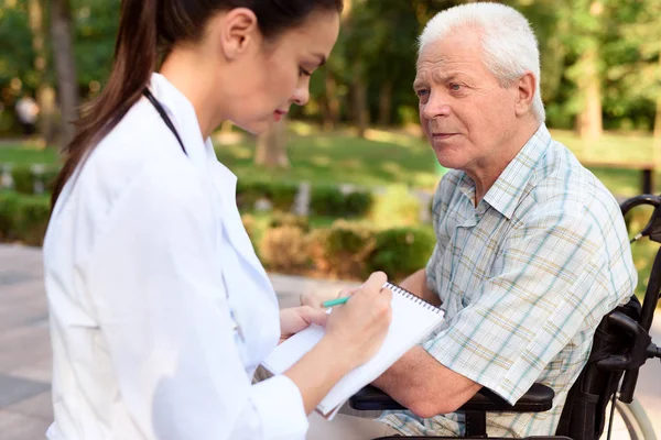 Doktor tıbbi kanıt yaşlı bir adamdan bir tekerlekli toplar — Stok fotoğraf