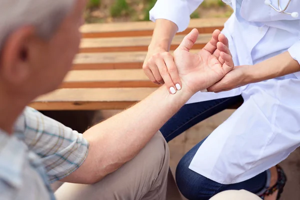 Lékař měří puls pacienta při posezení na lavičce v parku — Stock fotografie