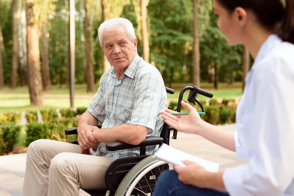 En äldre man i rullstol på en läkares mottagning i en sommar park — Stockfoto