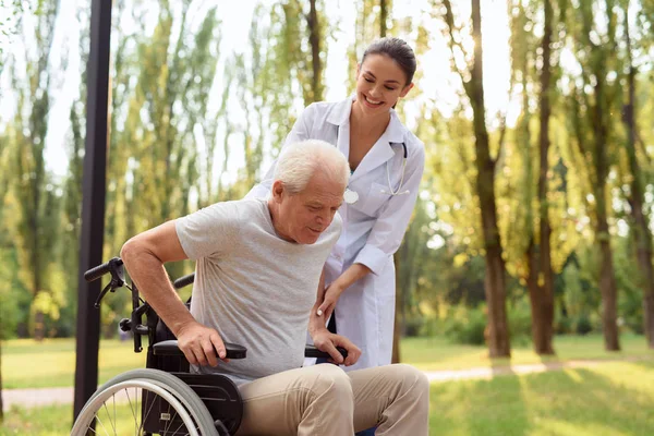 El cuidado ayuda a curar todas las dolencias. El médico ayuda al paciente a levantarse de la silla de ruedas —  Fotos de Stock