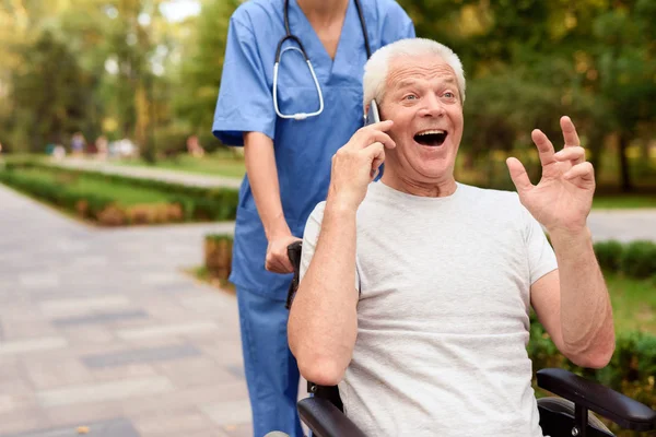 Gelukkig oude man zit in een rolstoel en gesprek met iemand aan de telefoon — Stockfoto