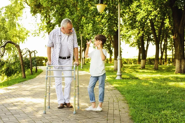 A boy and an old man on stilts for adults are walking in the park — Stock Photo, Image