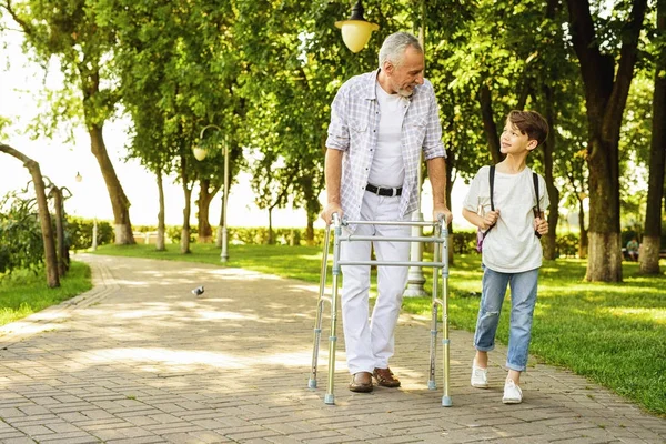 Chlapec a starý muž na kůlech pro dospělé jsou procházky v parku — Stock fotografie