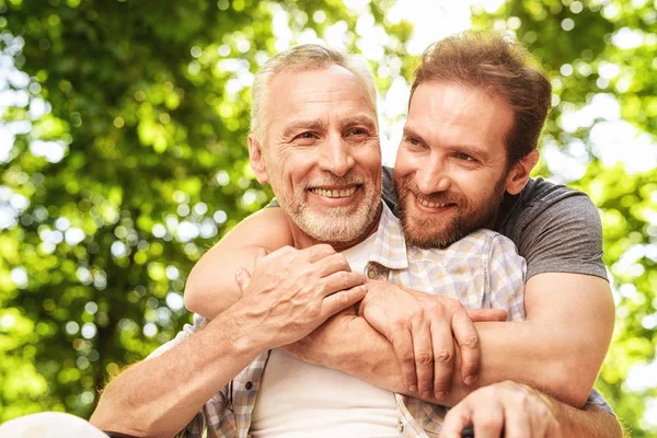 Den gamle mannen på en rullstol och hans son vandrar i parken. En man kramar sin äldre far — Stockfoto