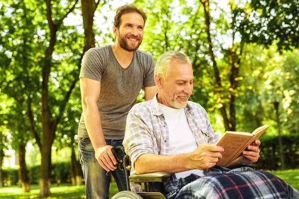 A man and an old man in a wheelchair in the park. The man covered the old man with a rug — Stock Photo, Image