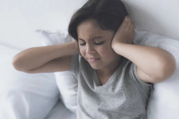 Una niña de pelo negro que yace en una cama blanca con las manos detrás de la cabeza — Foto de Stock