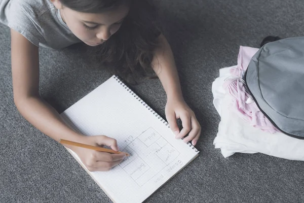 A lies on the floor next to her backpack with things and draws a pencil in a white notebook escape plan — Stock Photo, Image