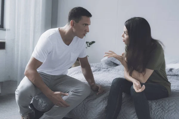 Um casal está sentado à beira de uma cama cinza em seu quarto e discutindo uns com os outros — Fotografia de Stock